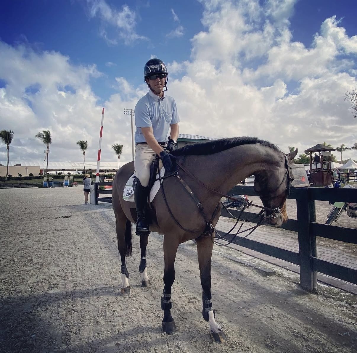 Kyle Gambino in show attire mounted on a horse at a Wellington venue, confident, looking toward camera with palm trees in background